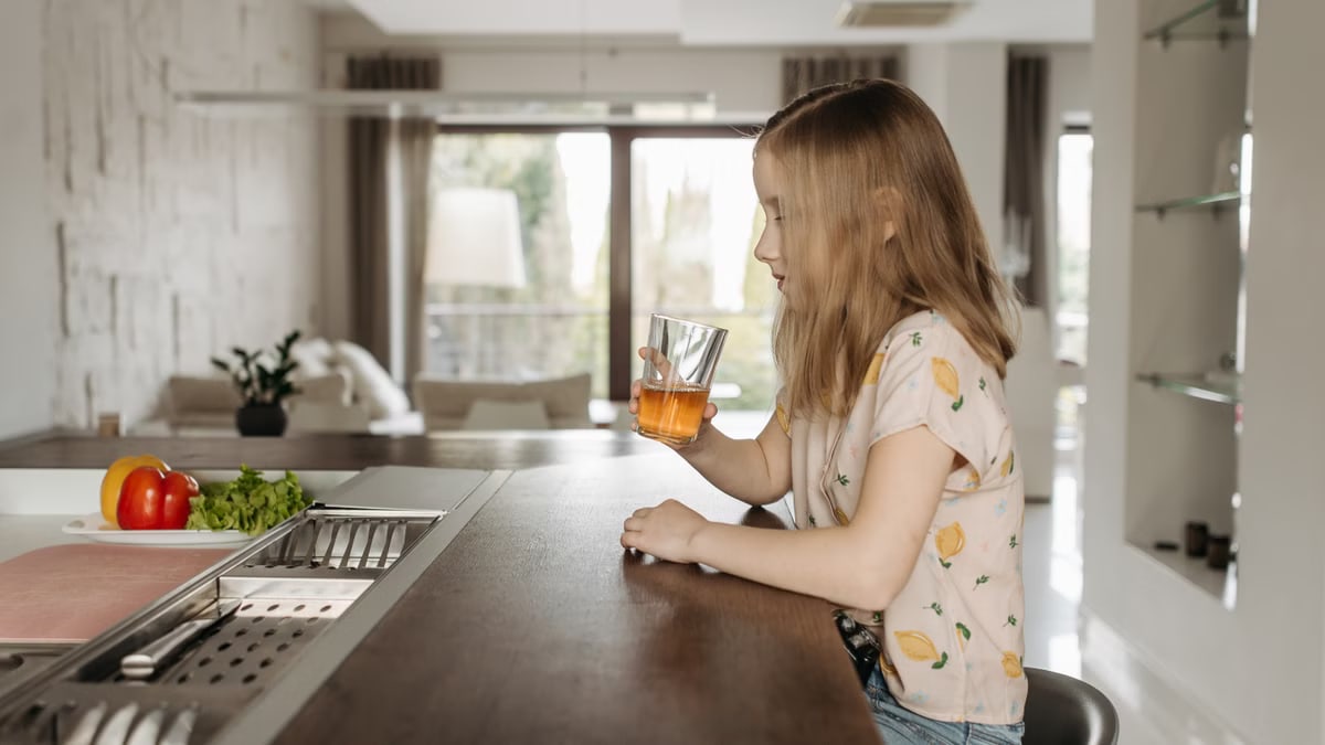 A young girl sitting at a modern kitchen counter enjoying a glass of juice.